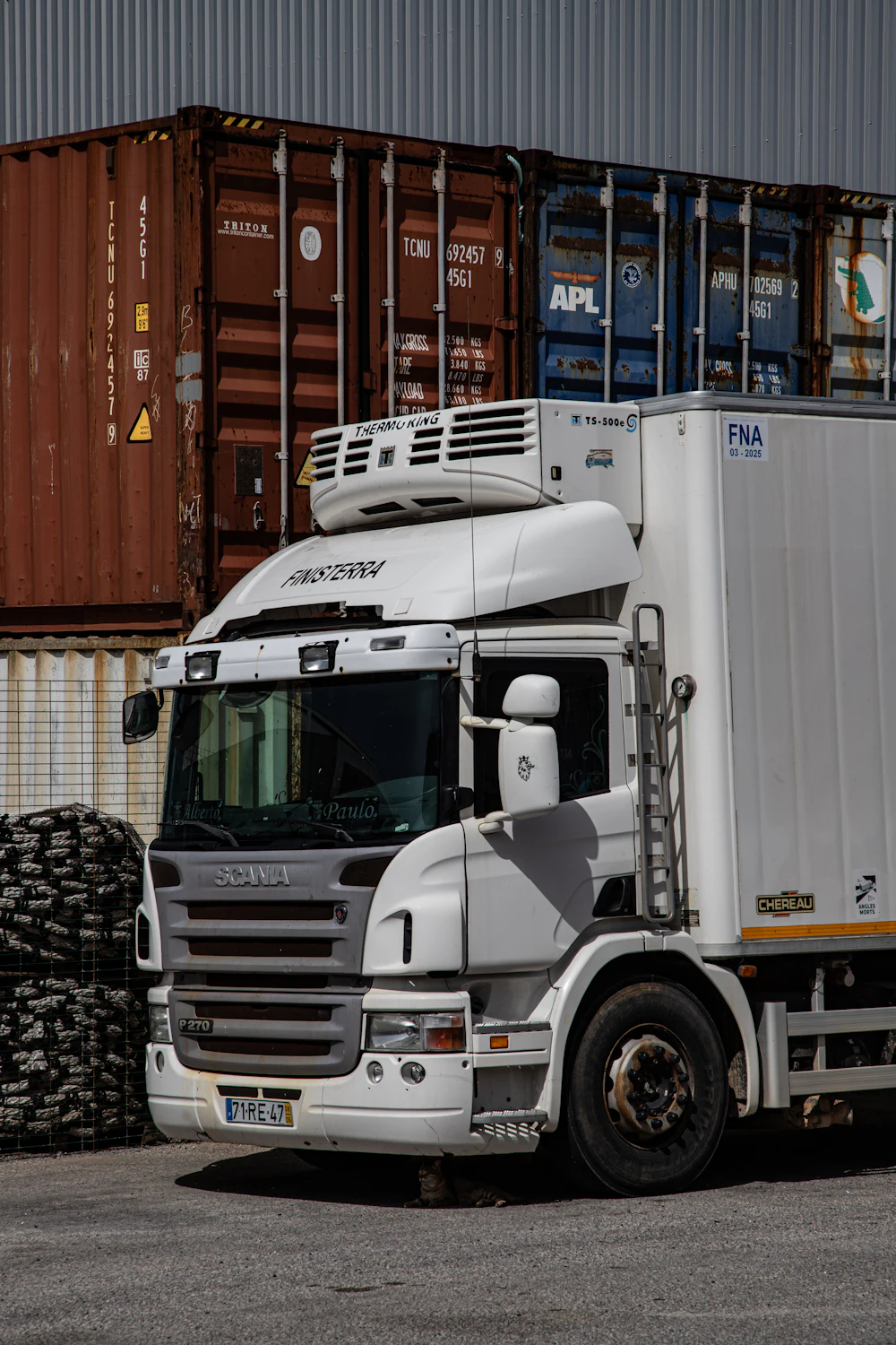 Refrigerated truck parked in front of containers on a logistics site
