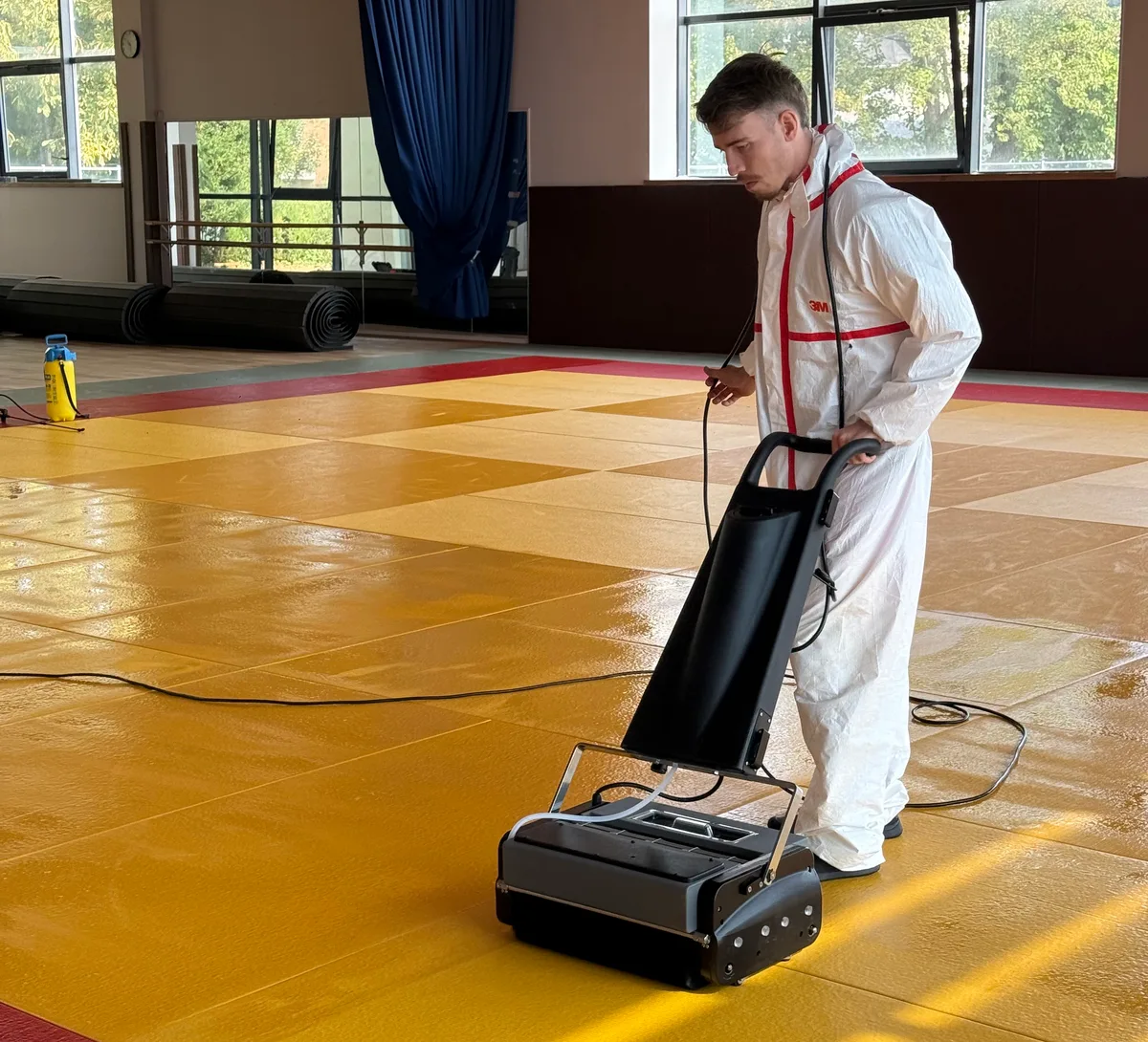 Nettoyage de tatamis dans une salle de sport avec une machine et une tenue de protection.
